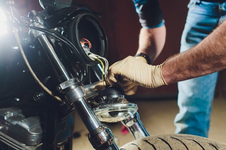 Man fixing bike. Confident young man repairing motorcycle near his garage. replacement lamp in the headlampの写真素材