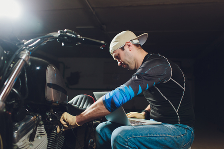 motorcycle mechanic repairing engine under supervisors guidance. video camera, laptop to view the inside of the engine to check soot.の写真素材