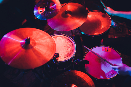 Drummer playing drum set at concert on stage. Music show. Bright scene lighting in club,drum sticks in hands.の写真素材
