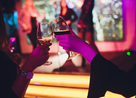 Young friends dancing with glasses of champagne in hands. Against lighting devices as background. Young peoples friends are dancing.の写真素材