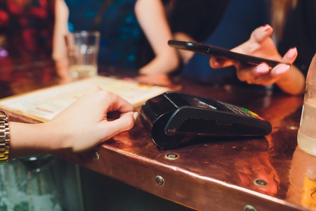 Mid-section of woman paying bill through smartphone using NFC technology in cafe.の写真素材