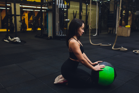 Muscular woman doing intense core workout in gym. Strong female doing core exercise on fitness mat with medicine ball in health club.の写真素材