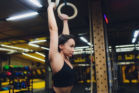 Young athletic sportswoman exercising on gymnastic rings at gym.