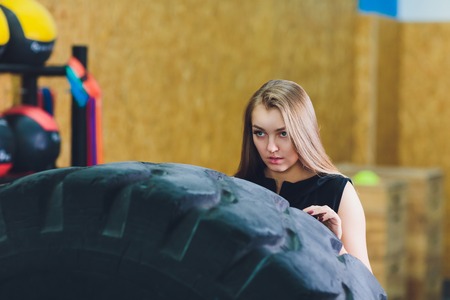 Fit female athlete working out with a huge tire, turning and carry in the gym. woman exercising with big tire.の写真素材