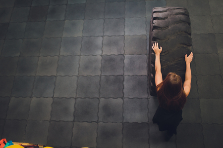 Fit female athlete working out with a huge tire, turning and carry in the gym. woman exercising with big tire.の写真素材