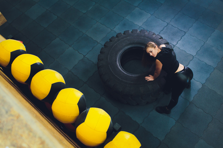 Fit female athlete working out with a huge tire, turning and carry in the gym. woman exercising with big tire.の写真素材