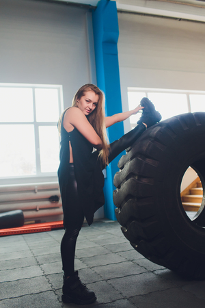 Fit female athlete working out with a huge tire, turning and carry in the gym. woman exercising with big tire.の写真素材
