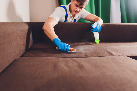 Cropped image. Cleaning concept. Male hand in protective gloves cleaning sofa couch in the room.の写真素材