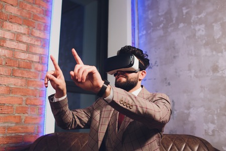 Closeup of male hand.Bearded young man wearing virtual reality goggles in modern coworking studio. Smartphone using with VR headset in office.の写真素材