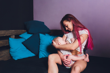 Mother breastfeeding baby in her arms at home. Beautiful mom Red hair breast feeding her newborn child. Baby eating mothers milk. Young woman nursing and feeding baby. Concept of lactation infant.の写真素材