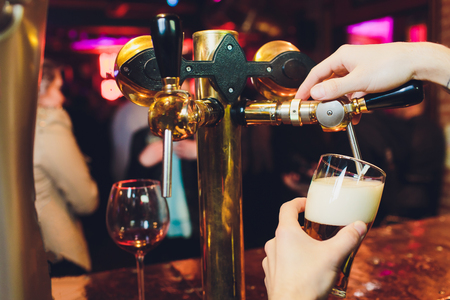 We meet oktoberfest. Hand of bartender pouring a large lager beer in tap. Pouring beer for client. Side view of young bartender pouring beer while standing at the bar counter.の写真素材