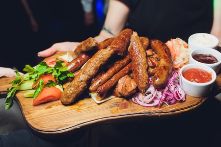 Male hands holding a iron tray with a meat for grilling. Sausages, steak and cevapi on a iron tray close up.の写真素材