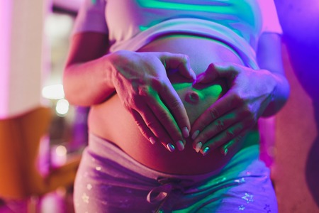 Pregnant Woman holding her hands in a heart shape on her baby bump. Pregnant Belly with fingers...