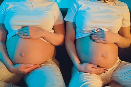 Two pregnant friends are waiting for their children showing belly.の写真素材
