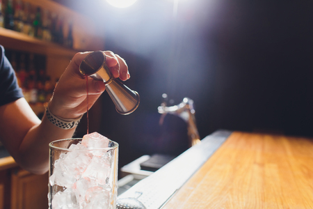 Barman in shirt and apron making an alcoholic drink with ice in a cocktail glass.の写真素材