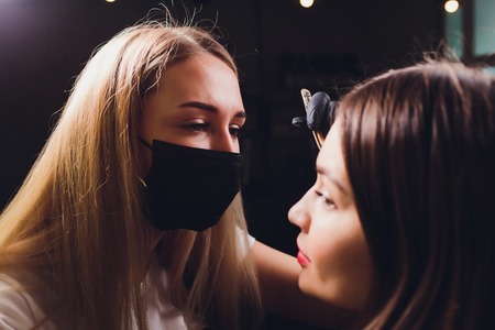 Cosmetologist making eyebrows design. Attractive woman getting facial care at beauty salon. Perfect architecture eyebrows.の写真素材