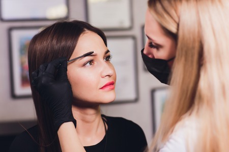 Cosmetologist making eyebrows design. Attractive woman getting facial care at beauty salon. Perfect architecture eyebrows.の写真素材