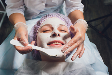 Beautiful european woman having facial skin procedure by applying a white rejuvenation mask by cosmetologist.の写真素材