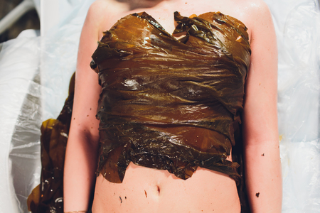 Spa treatment with algae. Woman on seaweed wraps at a spa salon. Firming procedure.の写真素材