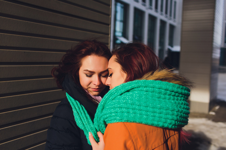 lesbian Couple of young women. Girl wears warm hat girl closes friends ears with her hands in mittens in cold winter.の写真素材