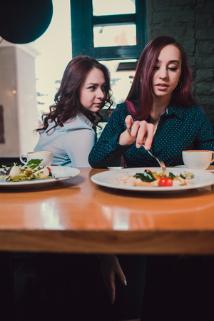Two unhappy lesbians not talking to each other after having quarrel during lunch at coffee shop: sad redhead woman feeling lonely while her girlfriend sitting next to her.の写真素材