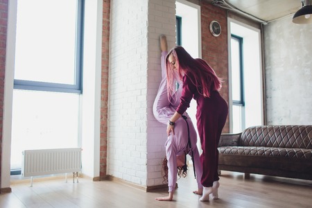 Professional two female athletes are sitting in yoga position together. They are touching their arms and looking at each other with serenity. Sunshine from big window.の写真素材