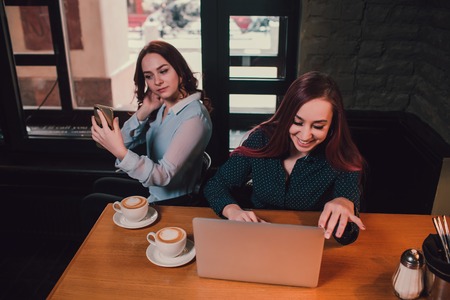 Two female students or lesbians having fun during coffee break at cafe, second half distract from work.の写真素材