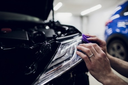 Worker hands installs car paint protection film wrap headlamp