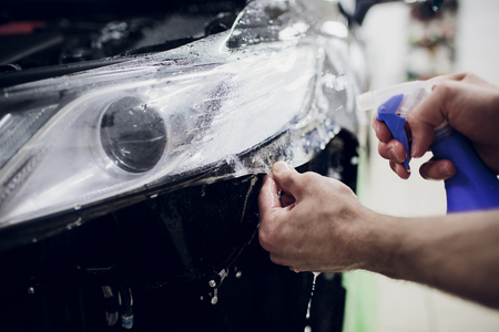 Worker hands installs car paint protection film wrap auto headlightの写真素材