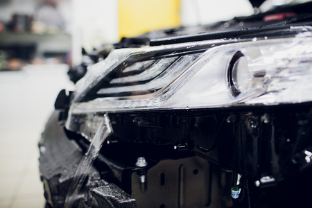 Worker hands installs car paint protection film wrap auto headlightの写真素材