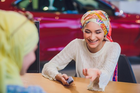 Beautiful woman enjoying happy moment getting car key from car seller auto salon. muslim woman in hijabの写真素材