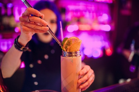 Bartender hand holding a glass with summer light sour cocktail with pink peach liquor decorated with flower under the bar counterの写真素材