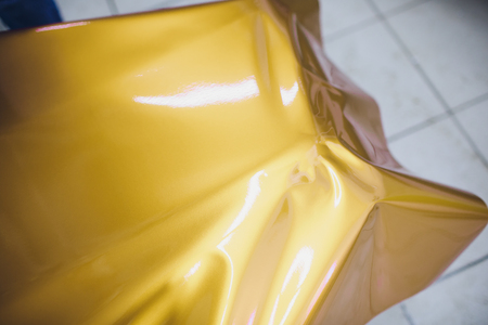 Car wrapping specialist putting vinyl foil or film on car wrapping protective film yacht, boat, ship, car, mobile home. yellow gold film hand pullsの写真素材