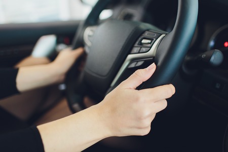 Female hands on the steering wheel of a car while driving. sunset the background, the windshield and...