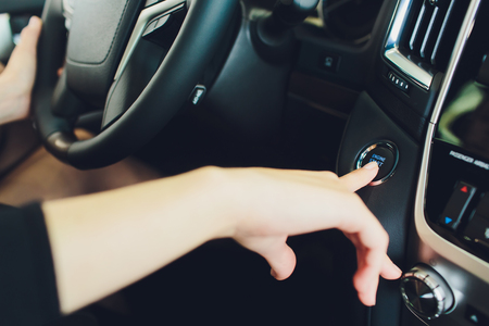 Woman starts the car engine with start-stop button. Modern car interiorの写真素材