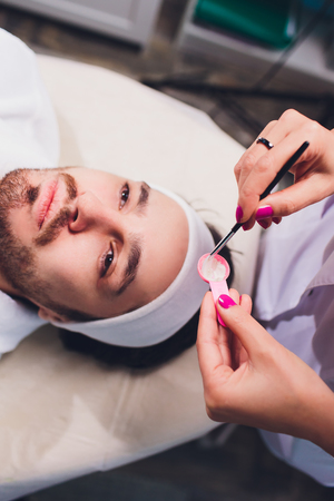 mens cosmetology. the doctor is a cosmetologist in a white robe, wearing gloves, puts a mask on the...