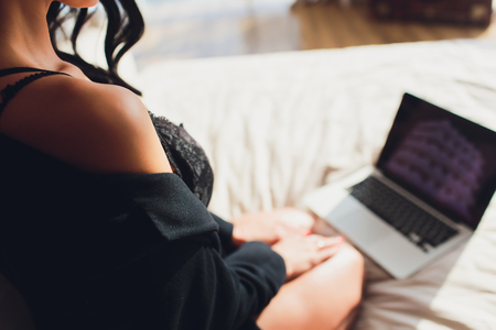 Beautiful, young girl posing in front of a web camera, working as a sexual model. The concept of online flirting, sex on the Internet.の写真素材