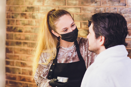 Professional barber in white shirt doing threading procedure and correcting shape of eyebrows to young male client sitting in chair in barber shop. Concept of styling and care.の写真素材