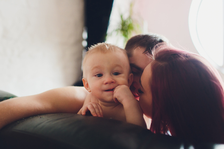 Happy parents with adorable little baby girl sitting on the couch at home, enjoying parenthood, young happy family, new life concept.の写真素材