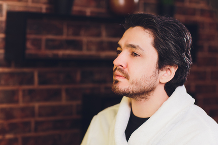 Professional barber in white shirt doing threading procedure and correcting shape of eyebrows to young male client sitting in chair in barber shop. Concept of styling and care.の写真素材