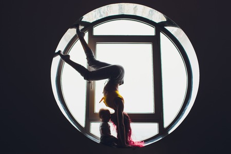 The dark silhouette of a beautiful woman with child on the background of the round window. yoga, acrobatics.の写真素材