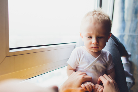 Loving mother playing with her baby sitting on a window.の写真素材