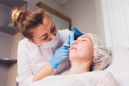 The doctor cosmetologist makes Lip augmentation procedure of a beautiful woman in a beauty salon.Cosmetology skin care.の写真素材