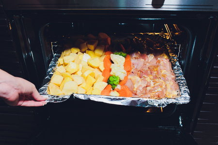 Cook taking ready fried baked chicken with vegetables from the oven. Home cooking concept.の写真素材