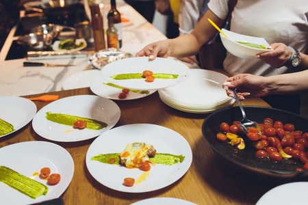 A male chef decorates a salad dish in a restaurant kitchen in a black apron. closeup of a hand with tongs.の写真素材