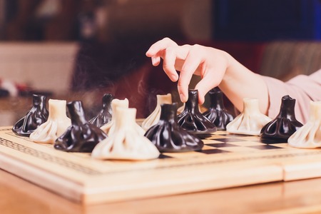 concept of Georgian cuisine. black and white khinkali stand on a chessboard. female hand takes...