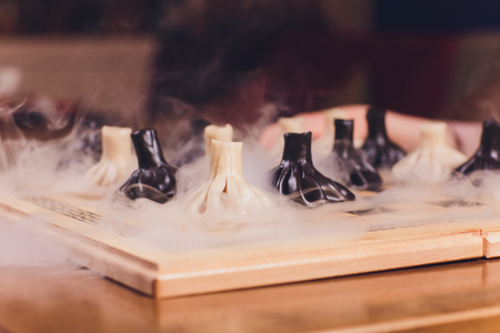 concept of Georgian cuisine. black and white khinkali stand on a chessboard. female hand takes khinkali. khinkali with barinas, veal and cheese.の写真素材