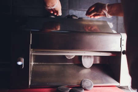 Chef making dough pastry sheeter bakery Baker forming shaping dough rolled pastry metal work table closeup hands process of preparing bread khinkali dough roller machine thin pasta sheet Top view. Blackの写真素材
