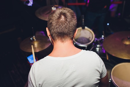 Drummer playing drum set at concert on stage. Music show. Bright scene lighting in club,drum sticks in hands.の写真素材