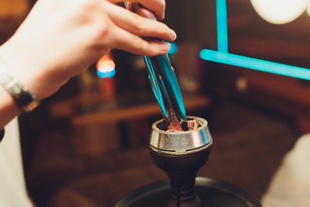 the guy changing the coals on the hookah in the hookah atmospheric.
